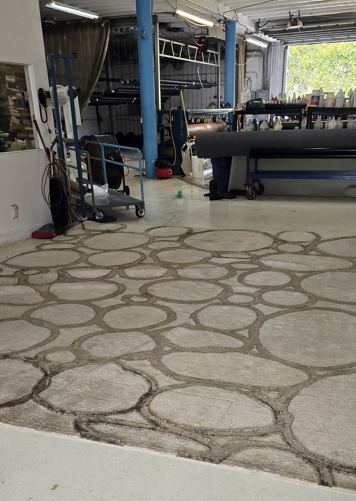 Large beige area rug with a circular pebble pattern laid out for inspection at Blue Steam's Delray Beach facility